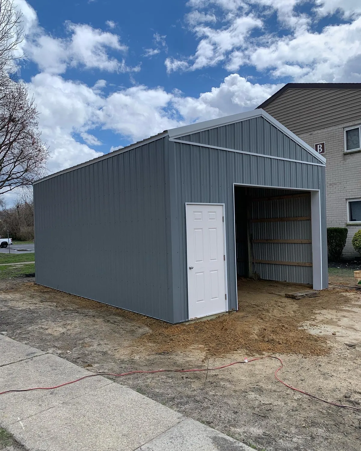 Gray single-bay pole garage with white entry door during construction