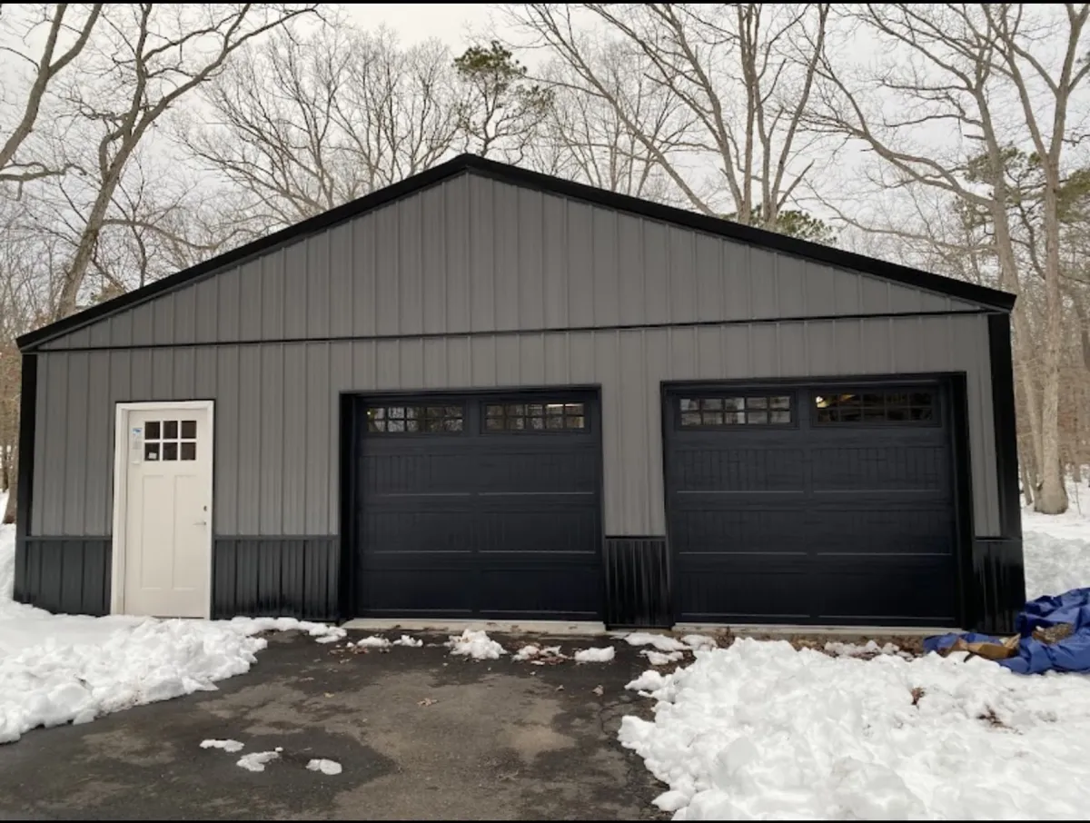 Gray two-bay garage with dark roof and trim in a snowy setting