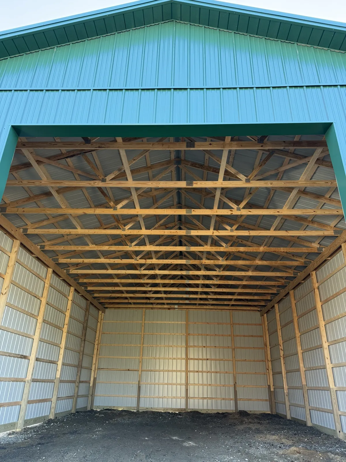 Exposed wood trusses and framing inside a green metal pole building