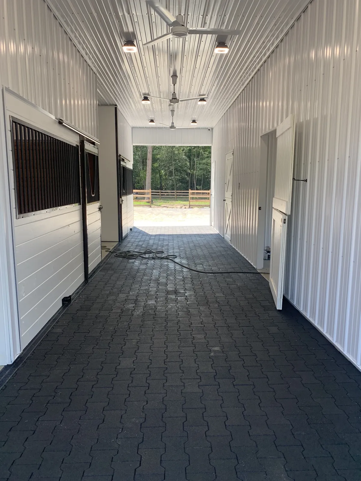 White horse barn aisle with stalls, ceiling fans, and paver flooring