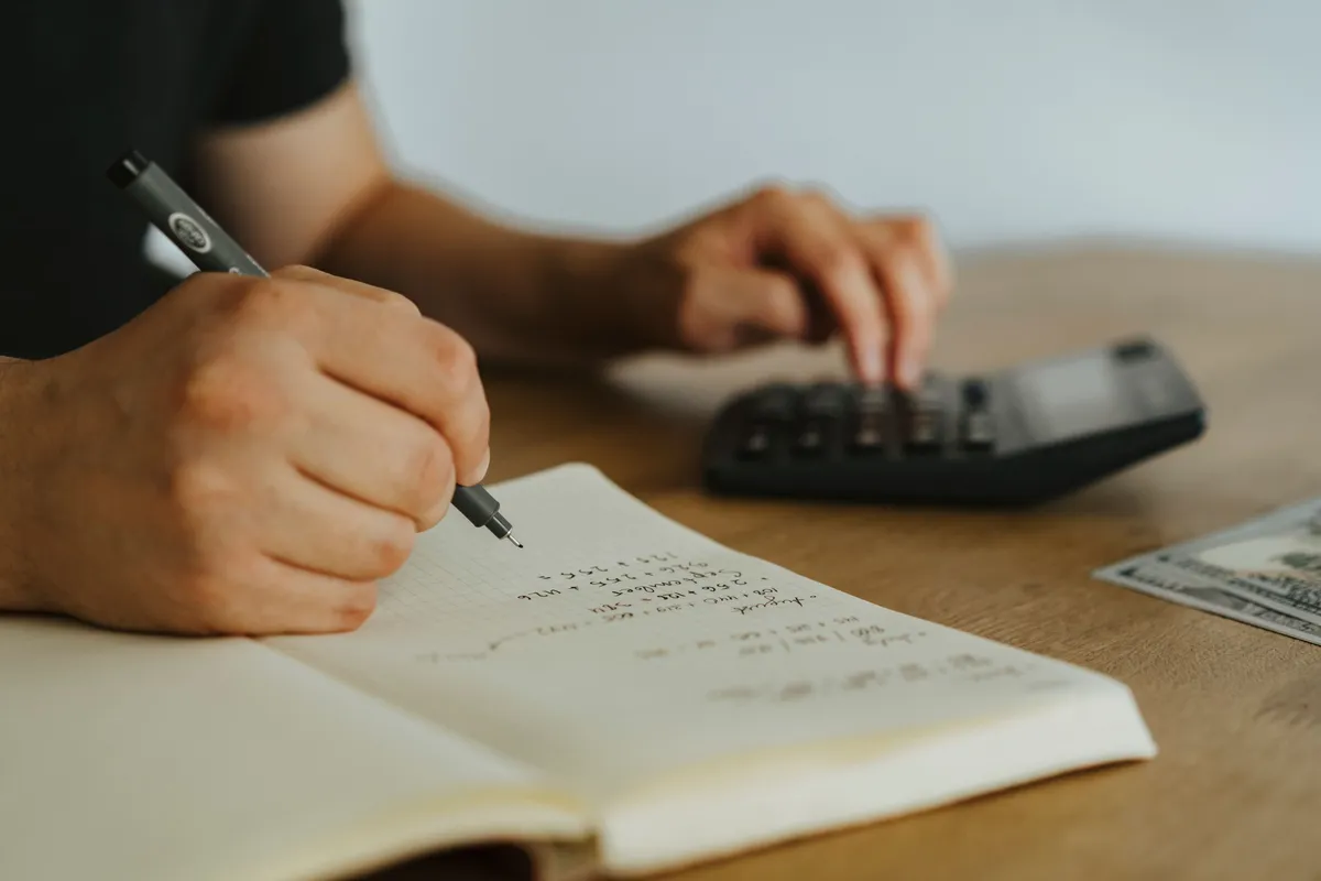 Person checking calculations in a notebook beside a calculator