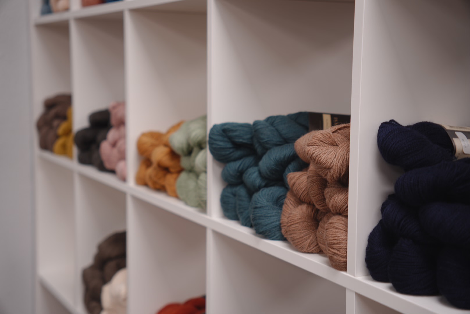 A close-up of hand-dyed skeins in rich, earthy tones, artfully arranged in a woven basket on a wooden table. The yarns have subtle color variations and soft textures, evoking a sense of artisanal quality and warmth.