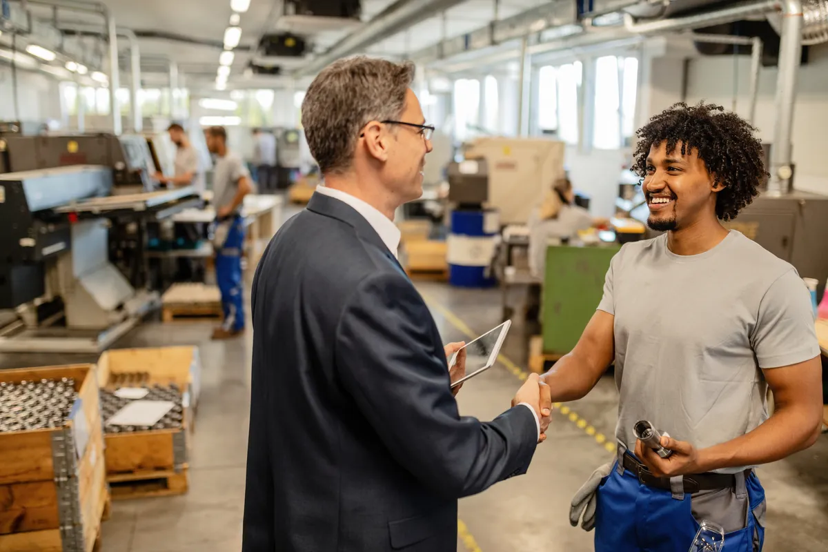 Factory manager and worker smiling and shaking hands
