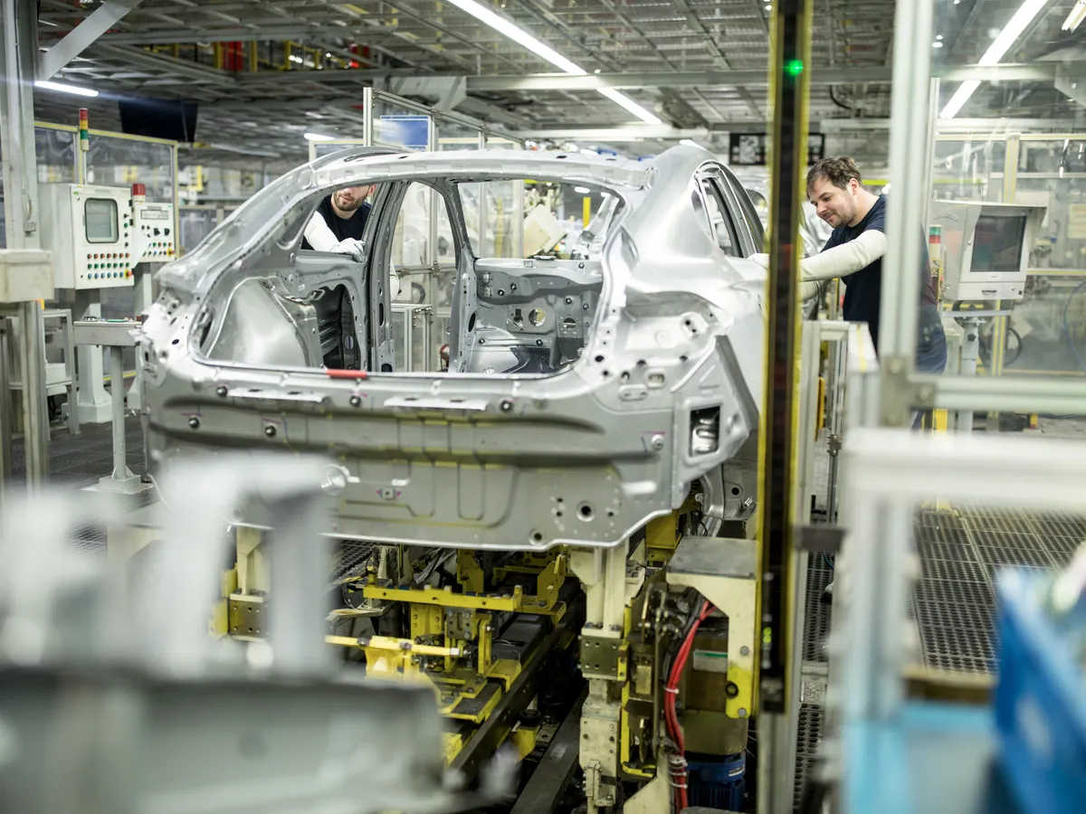 Two factory employees working on the chasis of a vehicle