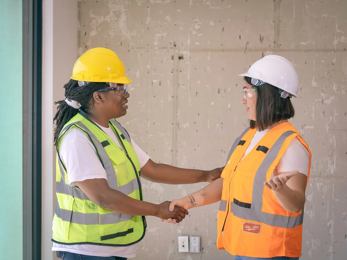 Two construction workers in hard hats and safety vests shaking hands
