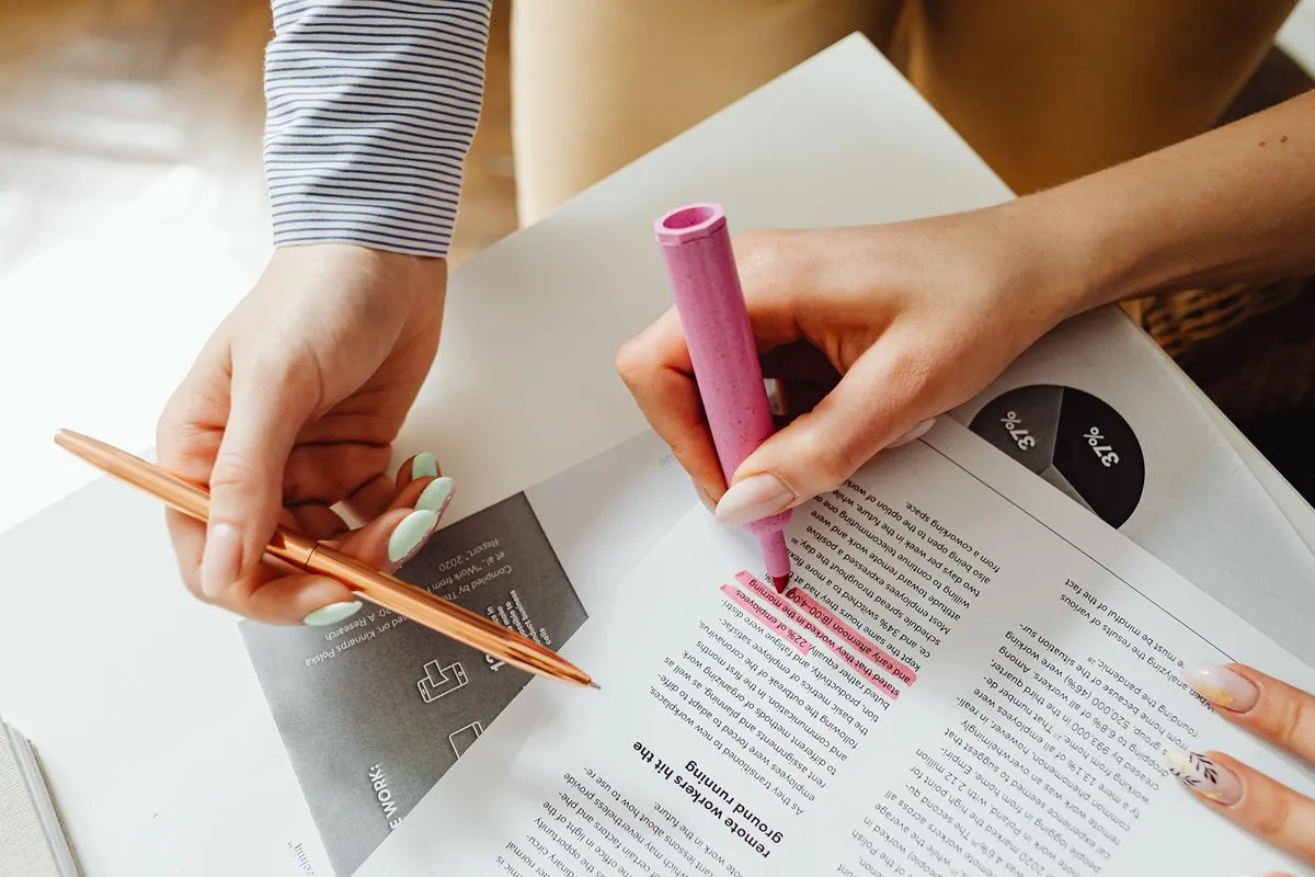 Hands marking key lines of a printed document with a highlighter and pen