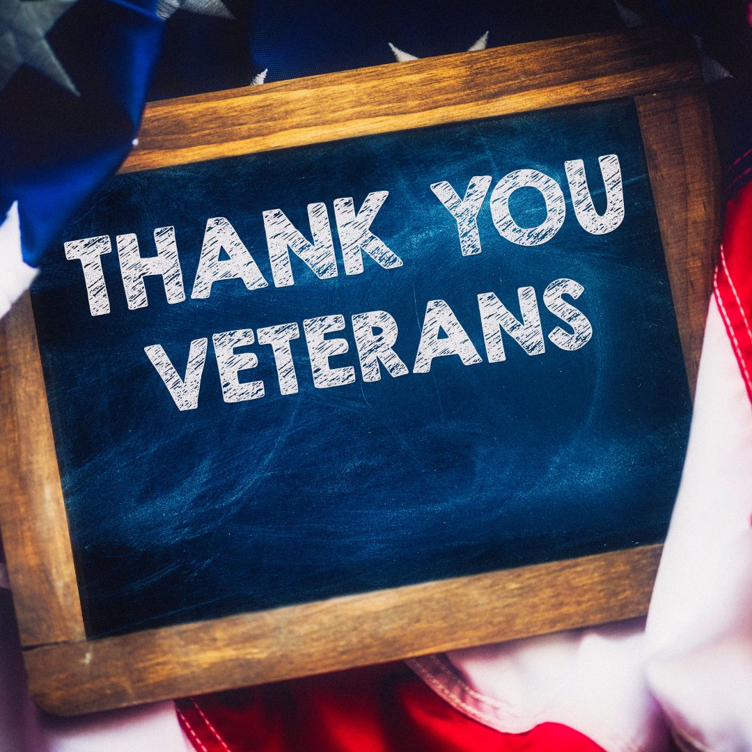 A wood-framed chalkboard with white chalk lettering, resting on a folded American flag. Text reads: THANK YOU VETERANS. Graphic by Jennifer Anne Garcia, Career Strategy Coach at bestresumecoach.com. #ThankYouVeterans #BestResumeCoach #CareerStorytelling