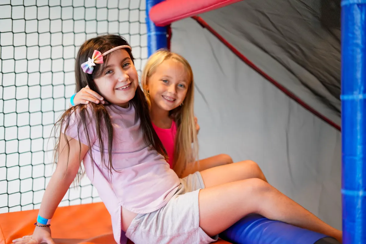 Two young girls smiling while sitting on the slide at Wild Child indoor playground in Bastrop