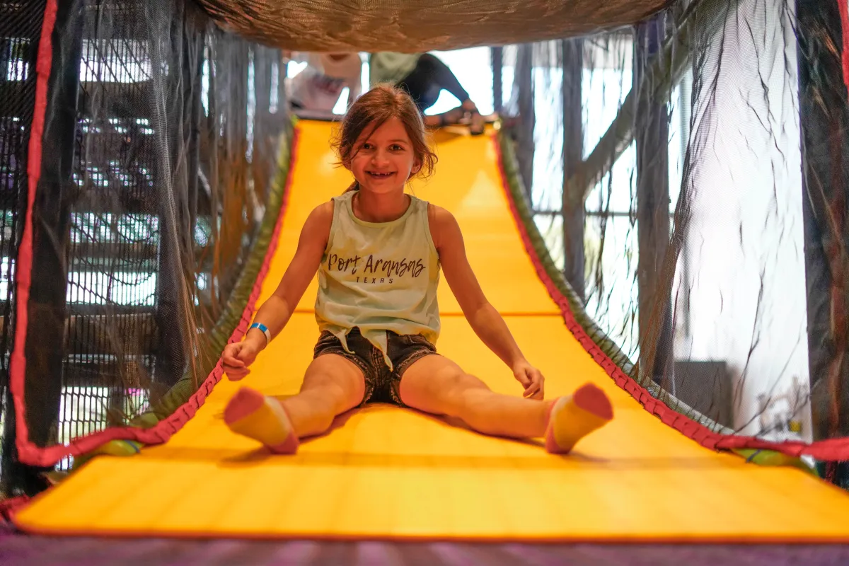 Young girl smiling as she slides down a colorful indoor playground slide at Wild Child in Bastrop