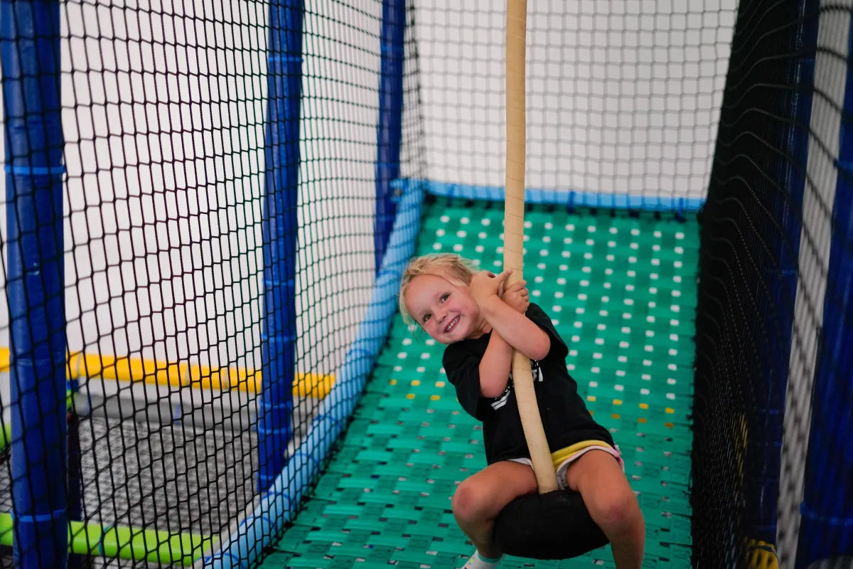Young girl swinging inside Wild Child indoor playground in Bastrop, TX