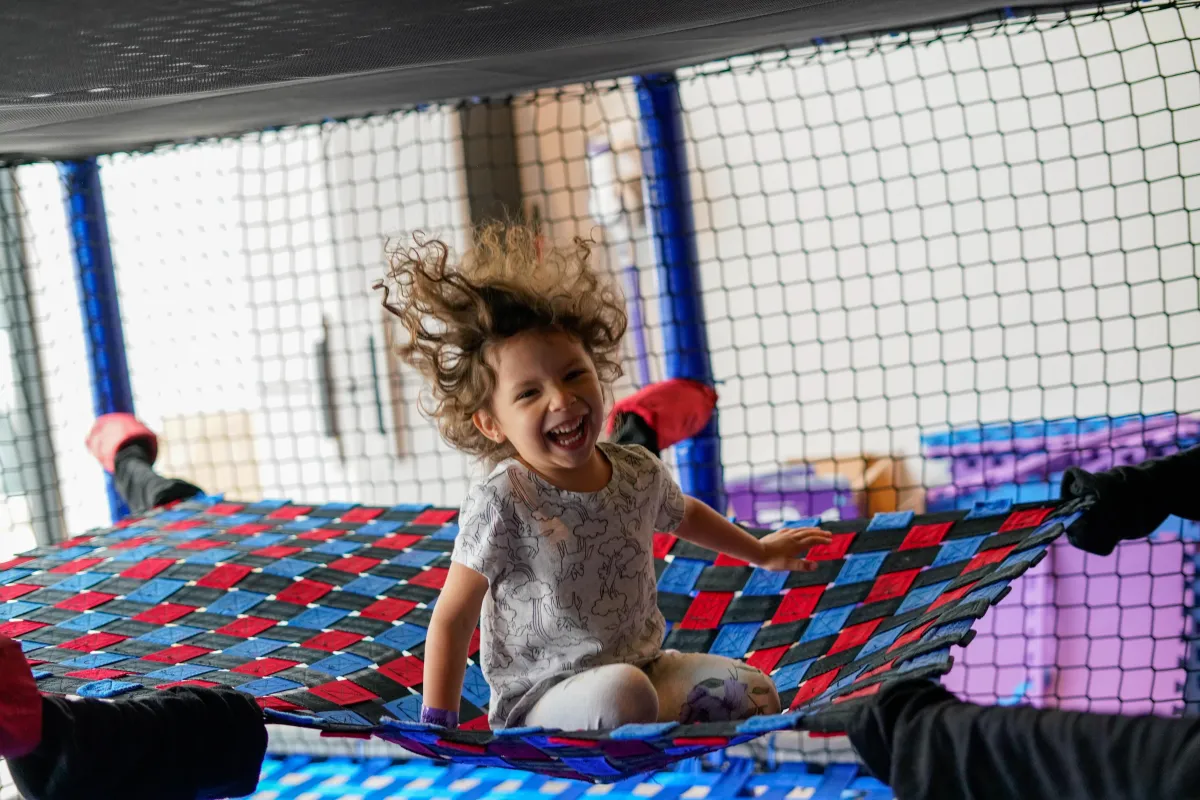 Girl bouncing on a hammock inside the Wild Child indoor playscape in Bastrop, TX