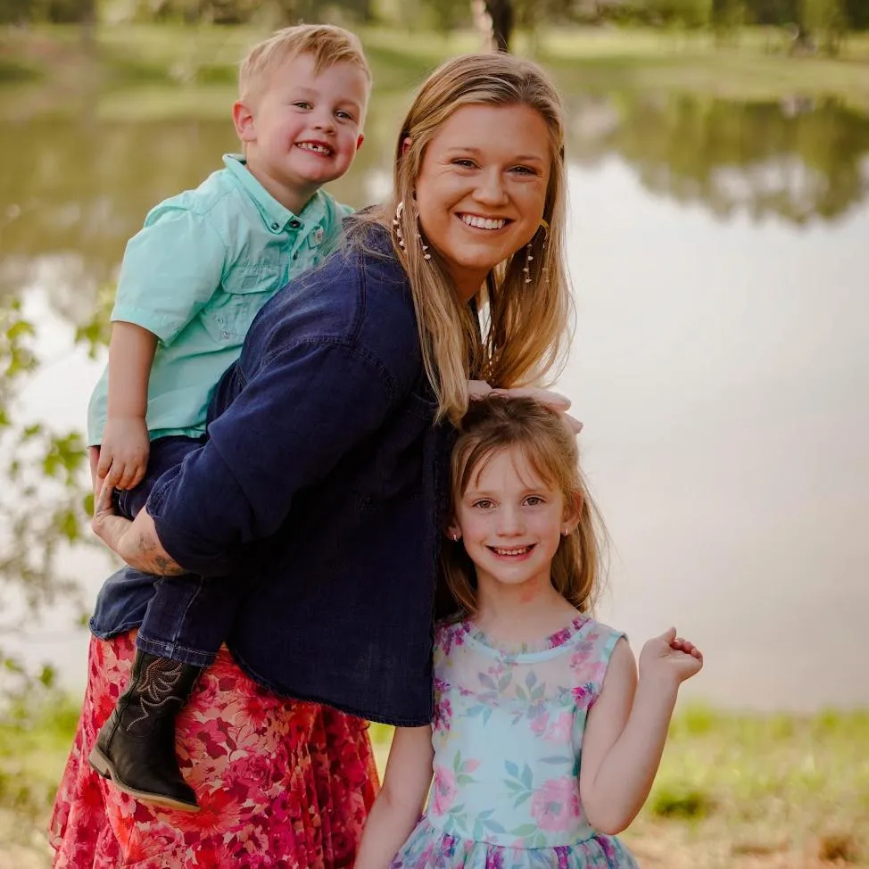 Nicole Woodall, play coach at Wild Child Bastrop, smiling with her two children outside