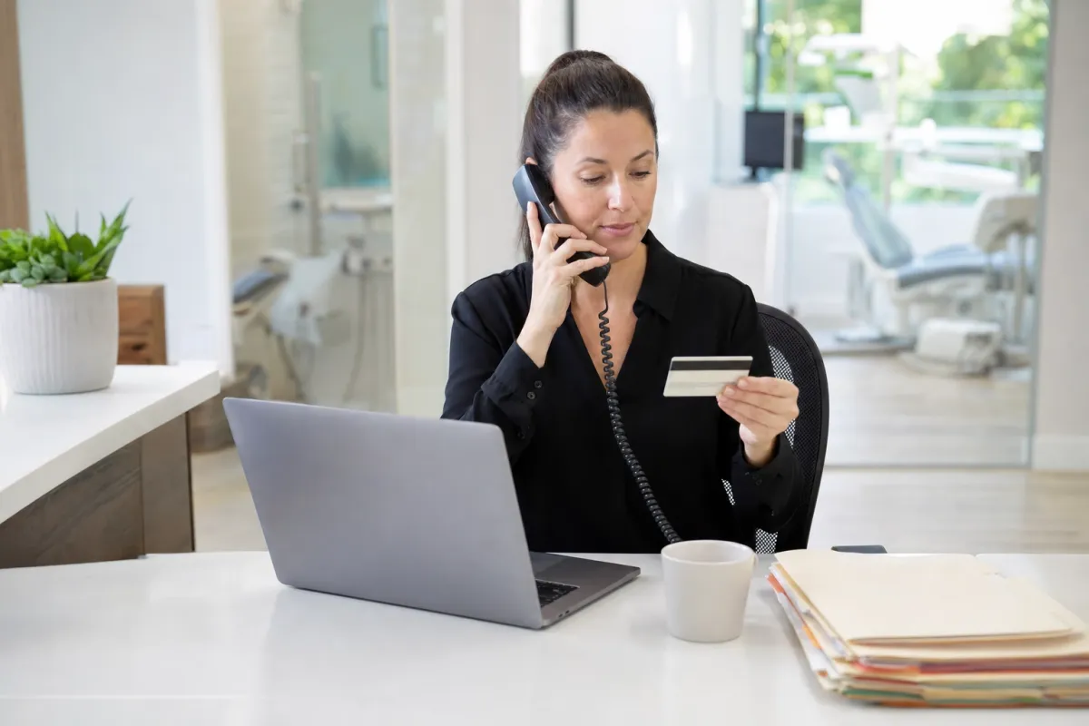 Dental office manager on the phone with MCNA Dental while holding a patient Medicaid dental card