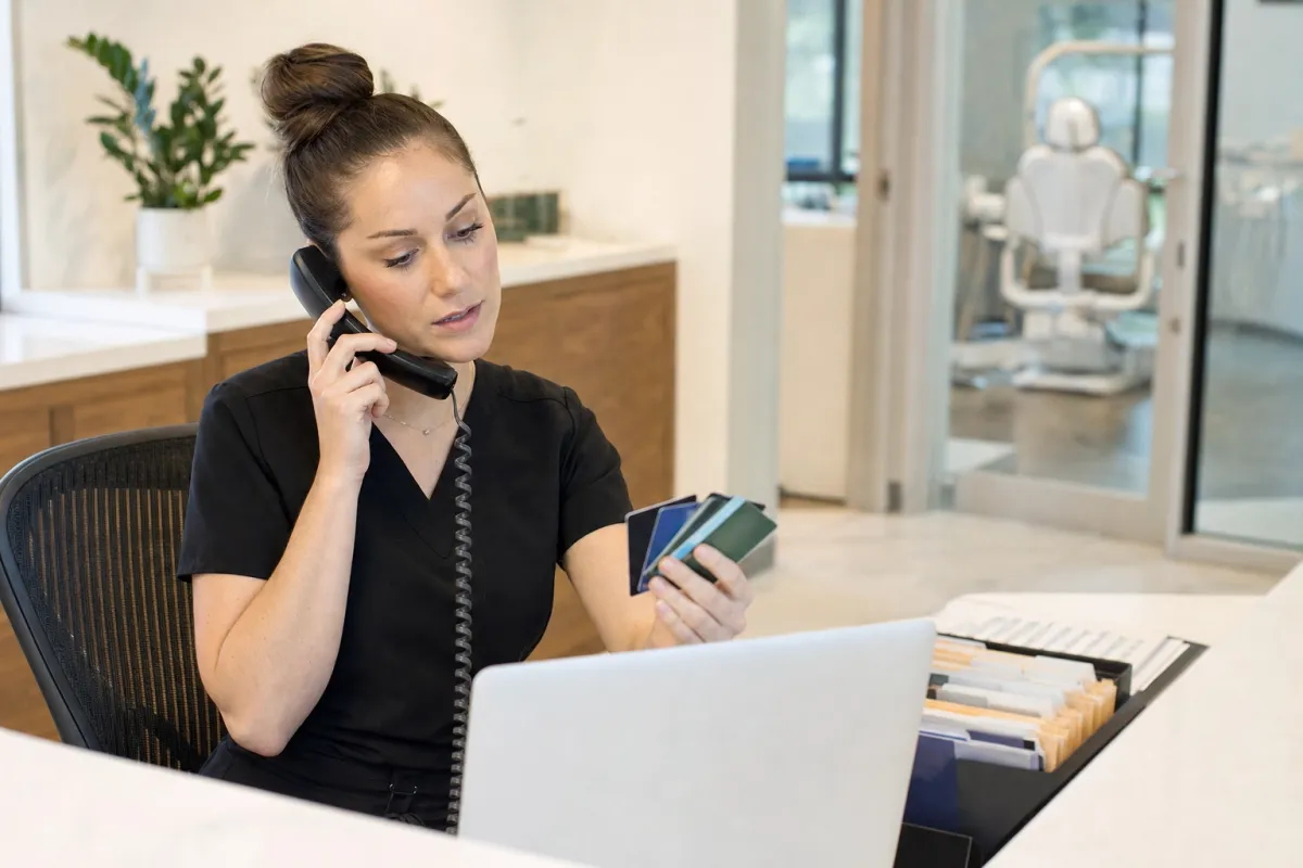 Dental billing coordinator on the phone holding several different dental insurance cards at a front desk