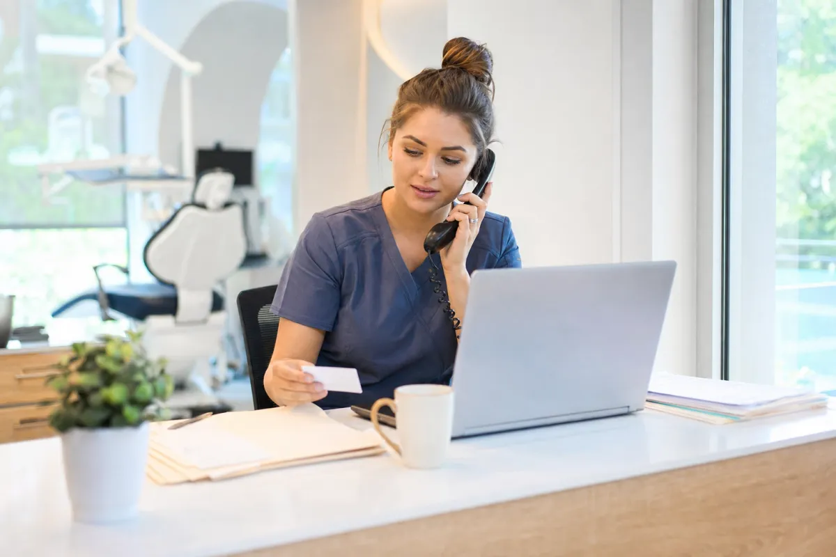Dental billing coordinator on the phone with MetLife while holding a patient insurance card