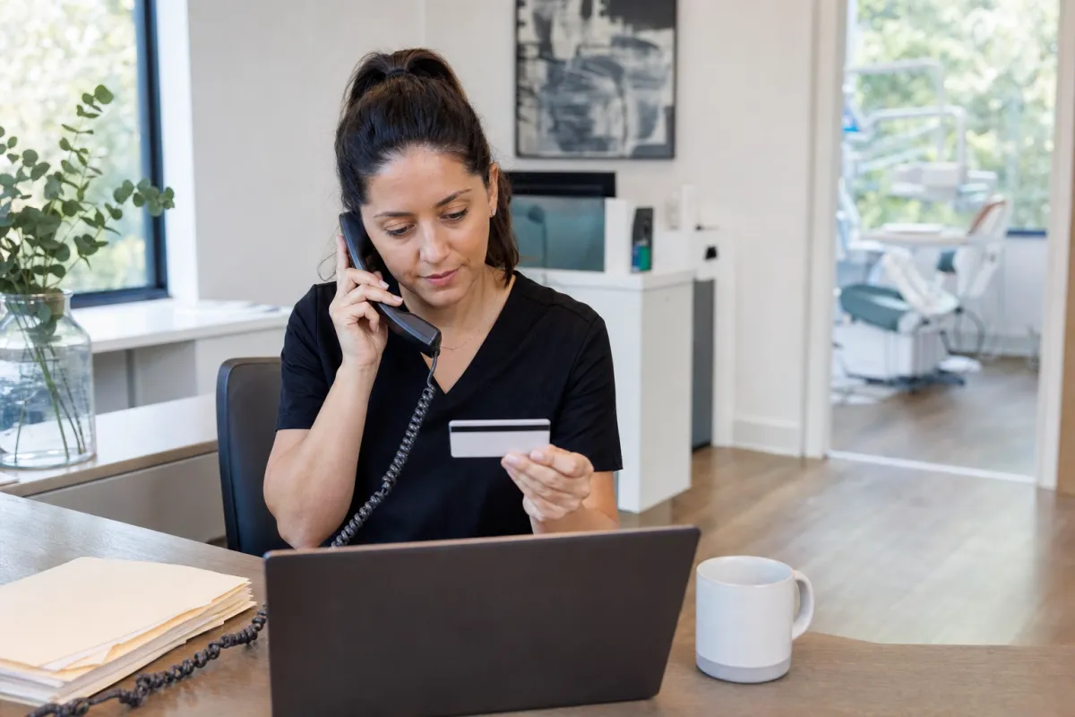 Dental office coordinator on the phone with GEHA dental while holding a patient insurance card