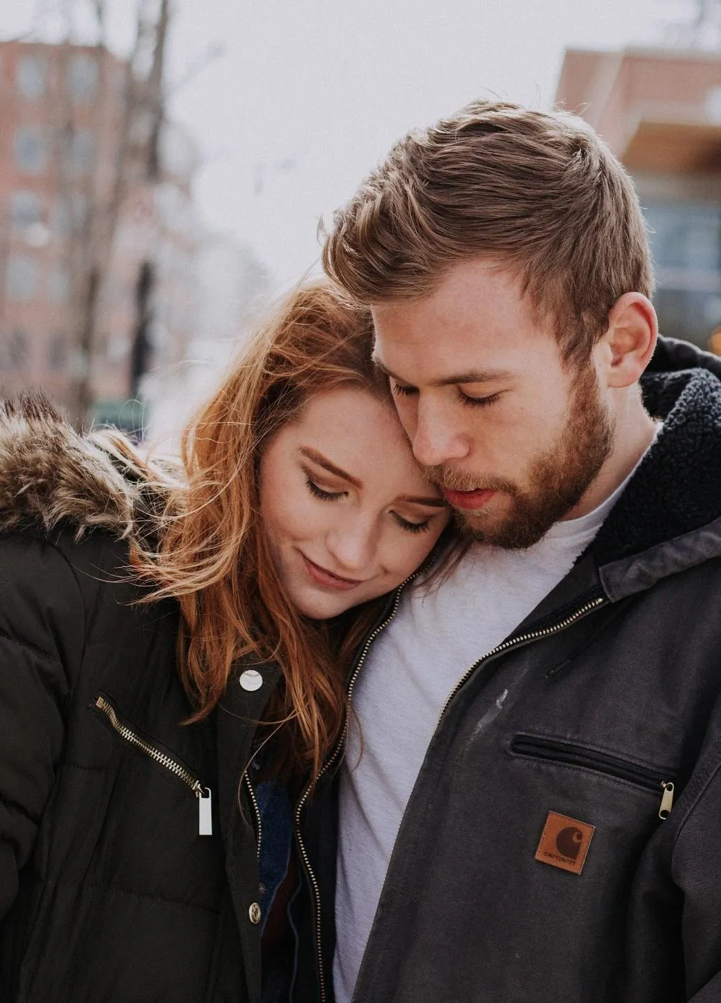 A couple embracing closely, heads gently touching as they look down, sharing a quiet, emotional moment.