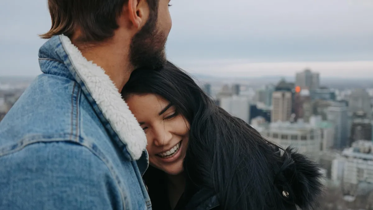 Femme souriante blottie contre son partenaire sur un toit avec vue sur la ville.