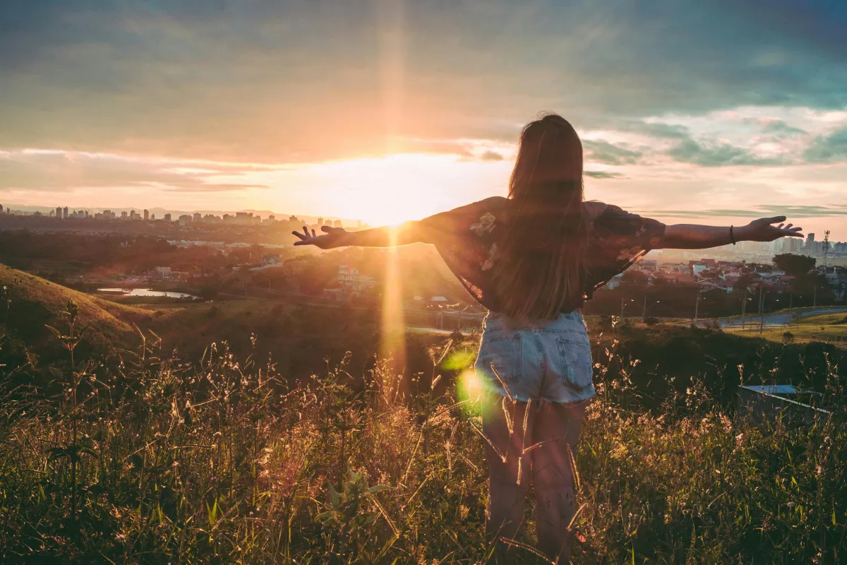 Woman standing in a field at sunset with arms raised, symbolizing empowerment and new beginnings.