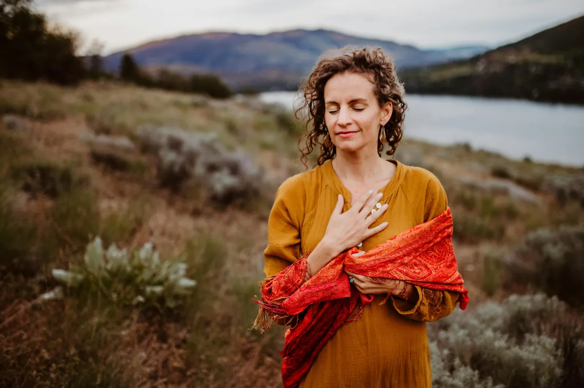 Woman standing outdoors with hand on heart, wearing a red shawl, evoking emotional healing and self-connection.