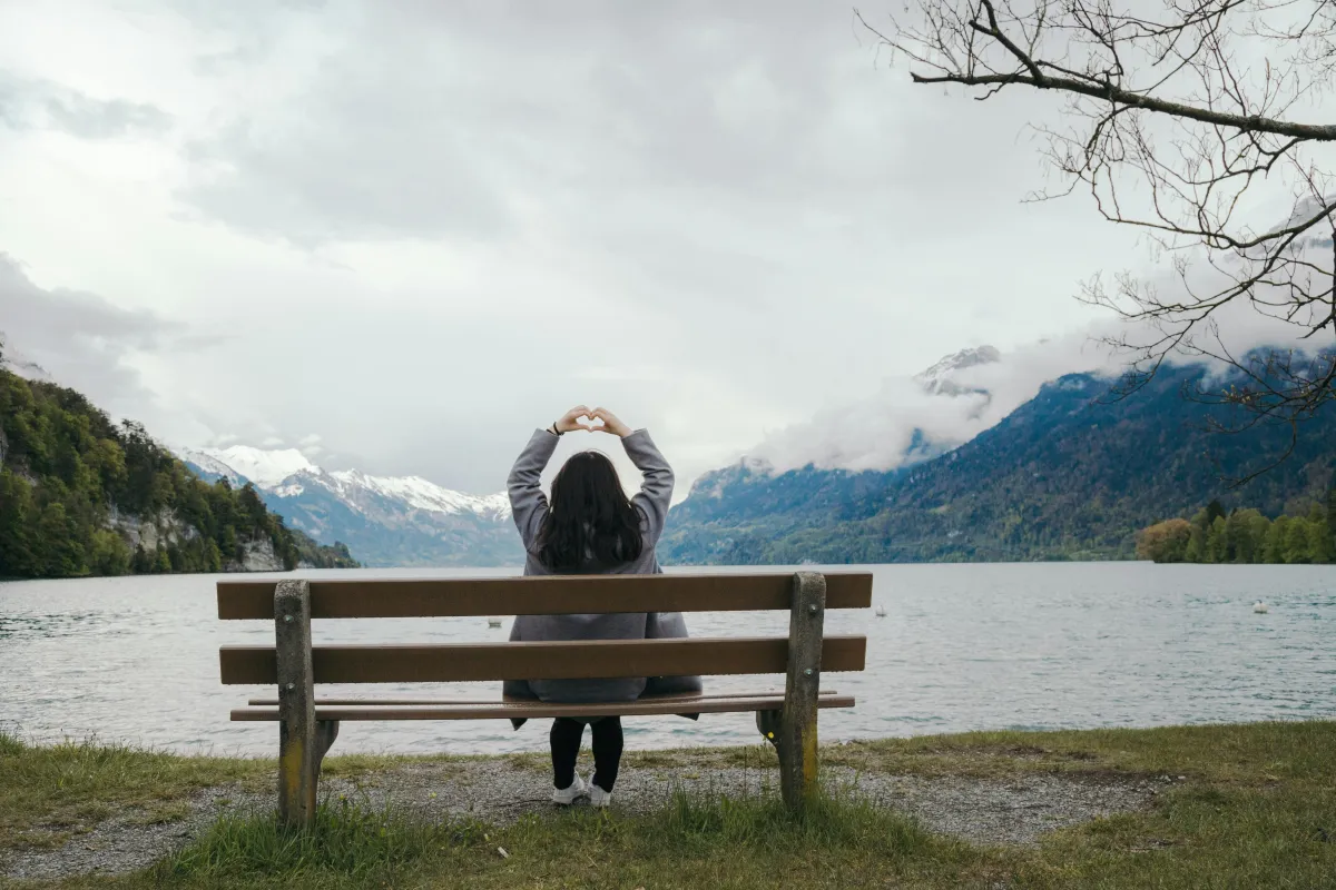 Person sitting on a bench facing a lake and mountains, representing personal reflection and inner growth.