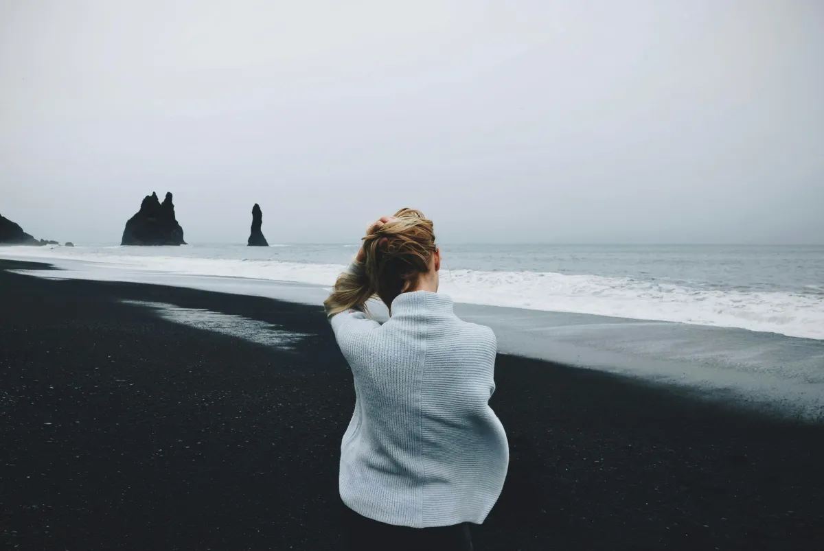 Woman sitting by the ocean, holding her hands, looking out at the water.