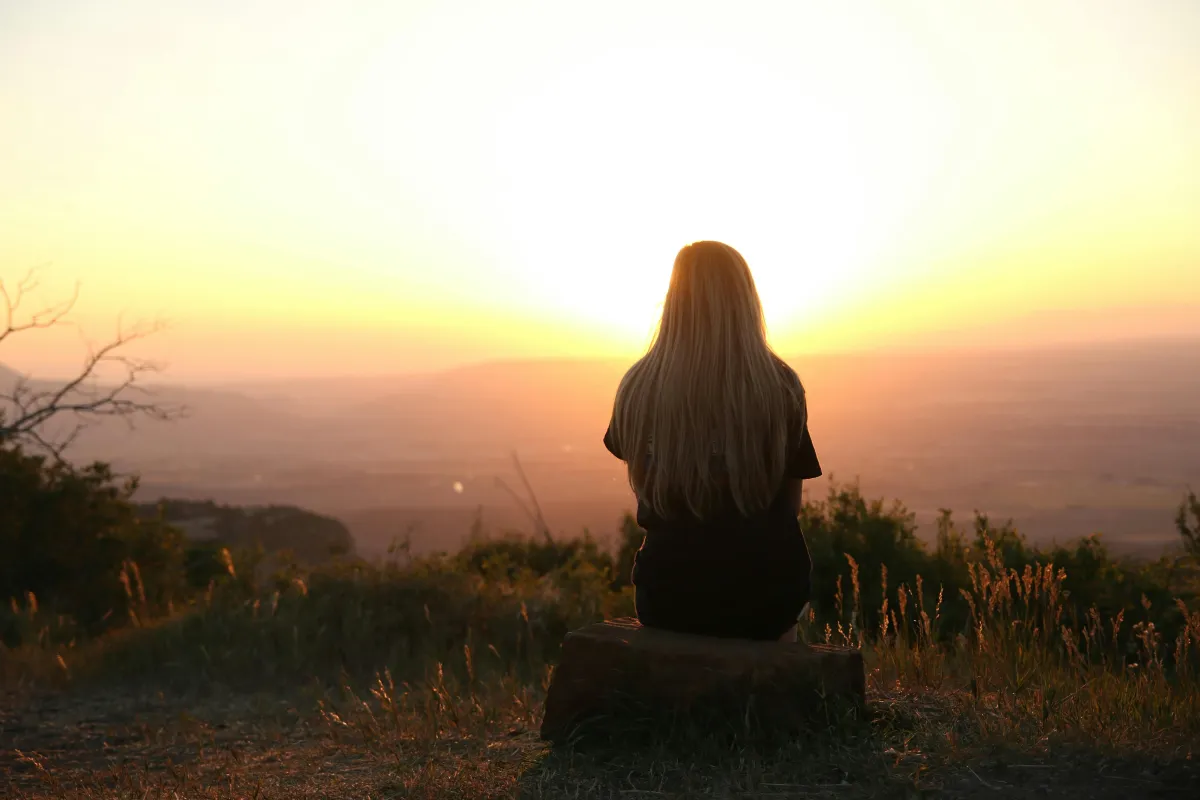 Woman sitting on mountaintop at sunset, gazing at the horizon.