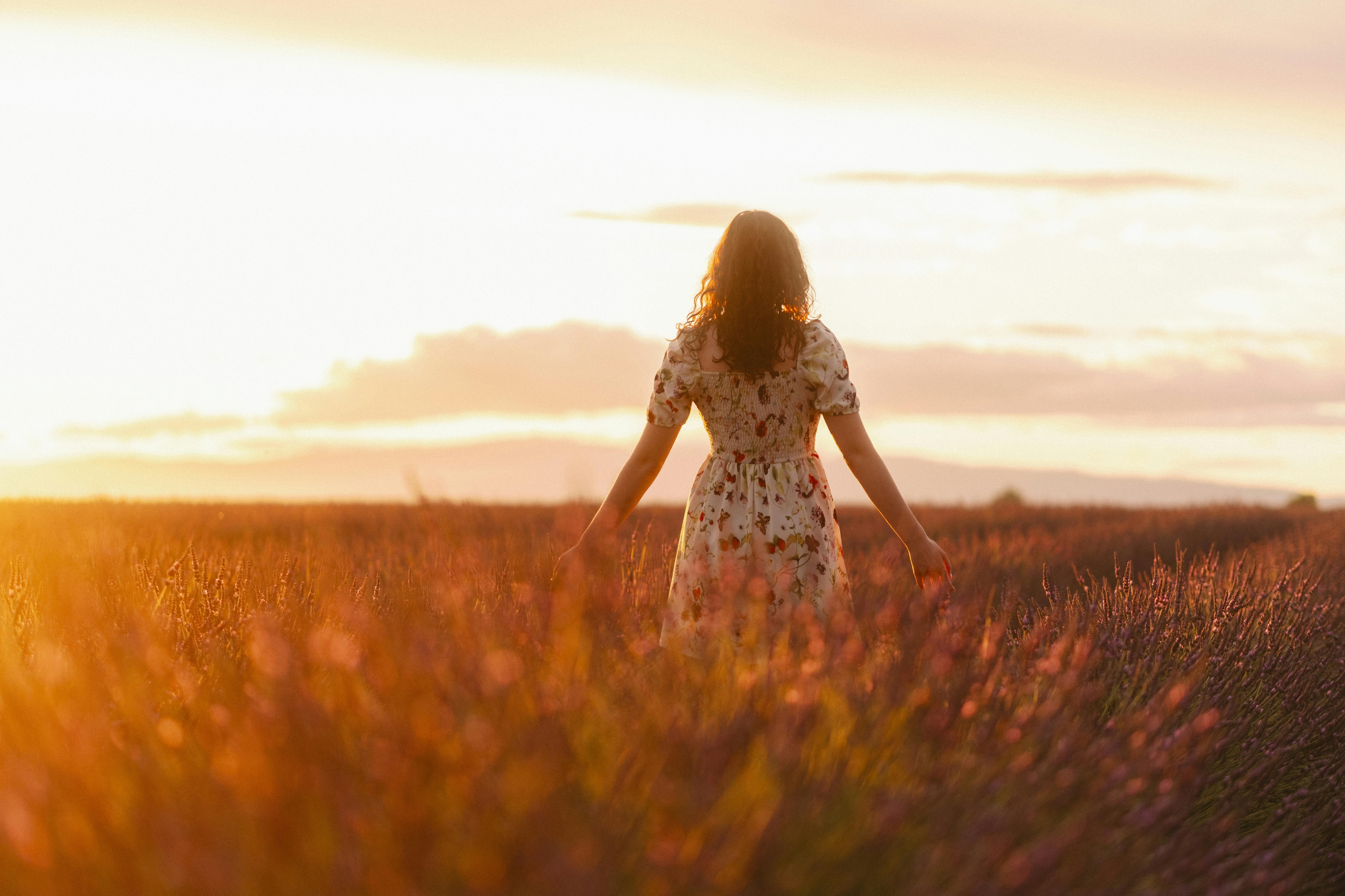 Woman in a floral dress standing in a glowing sunset field, symbolizing self-discovery, personal growth, empowerment, and emotional healing journey.