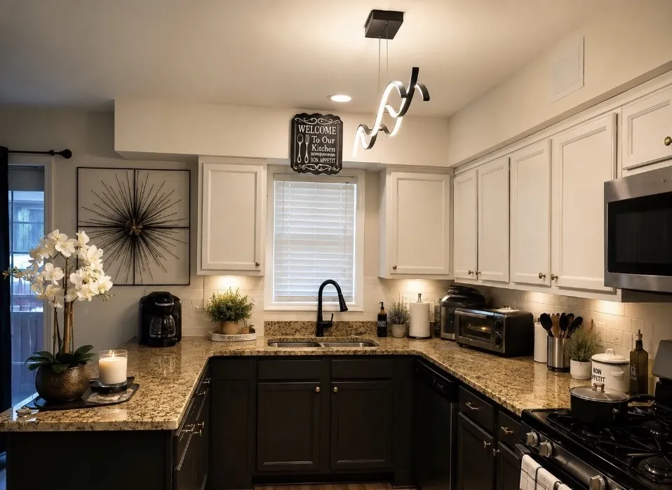 Modern kitchen with white upper cabinets, black lower cabinets, granite countertops, black fixtures, warm lighting, and decorative accents.