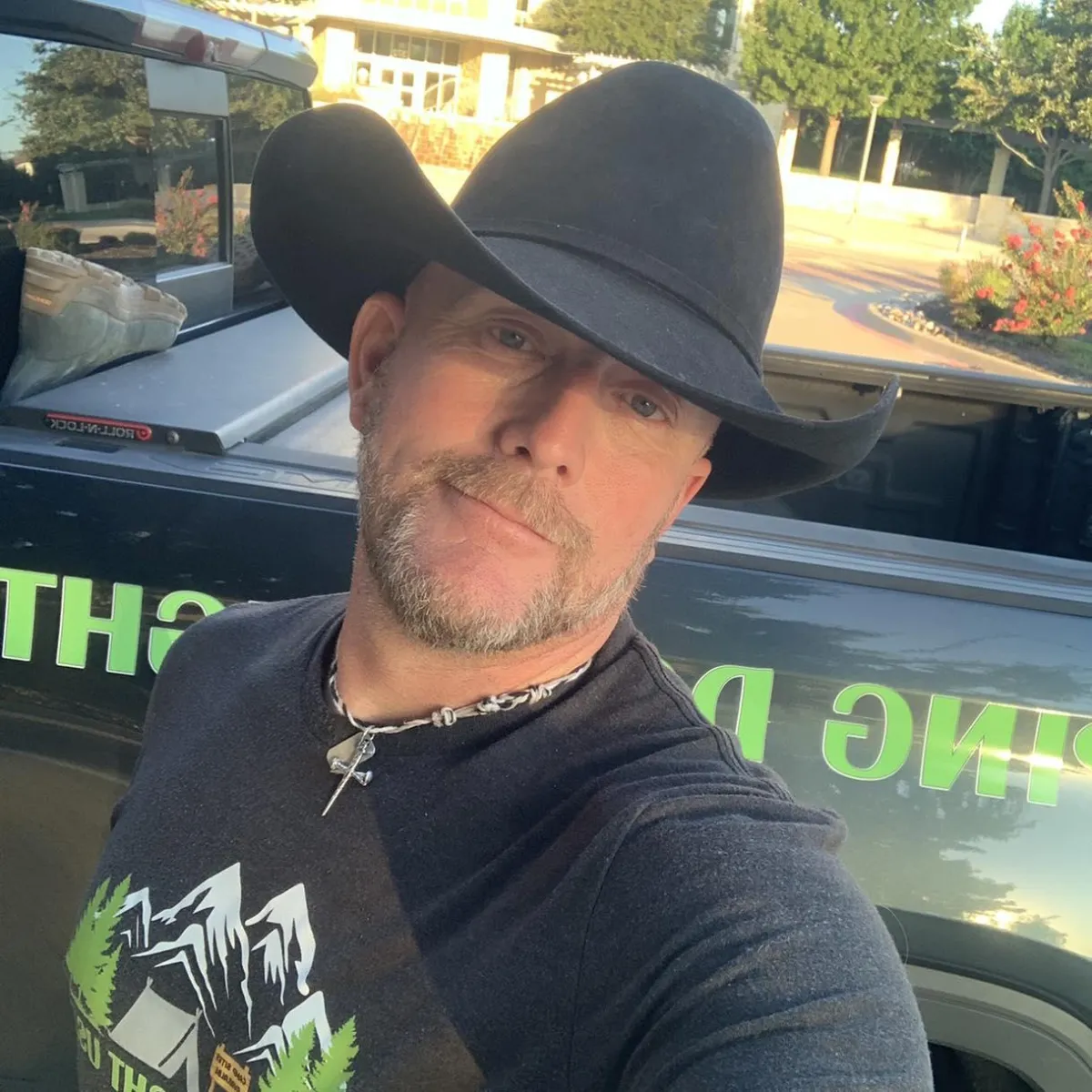 A man wearing a cowboy hat is seated inside a car, looking relaxed and enjoying the view from the driver's seat