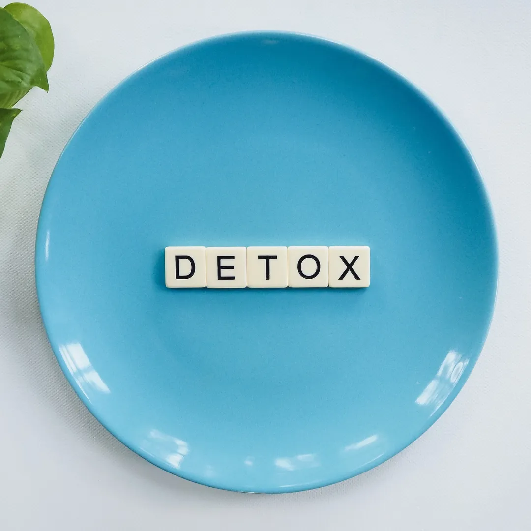 Scrabble tiles spelling “DETOX” on a blue plate, illustrating natural detoxification options with homeopathy