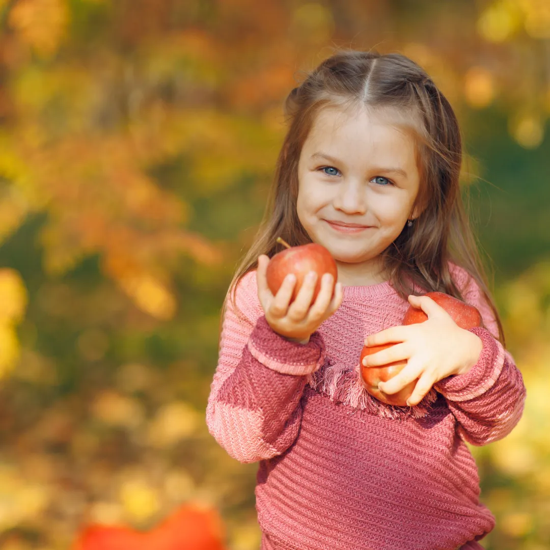 Smiling young girl holding apples in an autumn park, symbolising holistic support for children with PANS/PANDAS through homeopathy
