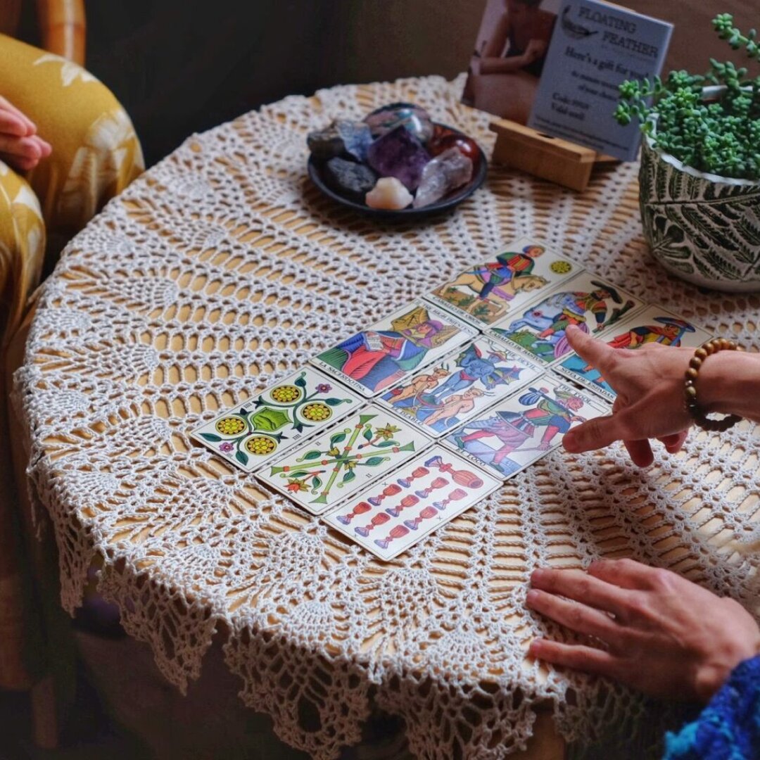 Hands interacting with Tarot cards laid out on a lace-covered table beside crystals—symbolising intuitive, grounded guidance sessions offered in Brighton for emotional clarity and self-reflection.