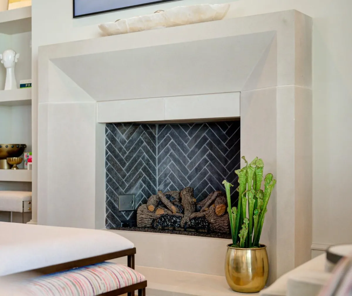 A modern Angolo design fireplace featuring a light stone mantel and a dark herringbone tile interior.