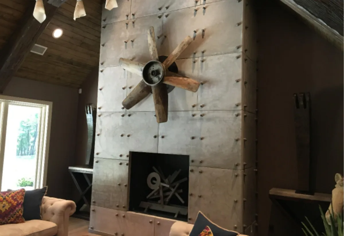 The bold Stone Lucido fireplace, featuring a floor-to-ceiling industrial design of riveted panels and a rustic wooden propeller accent.