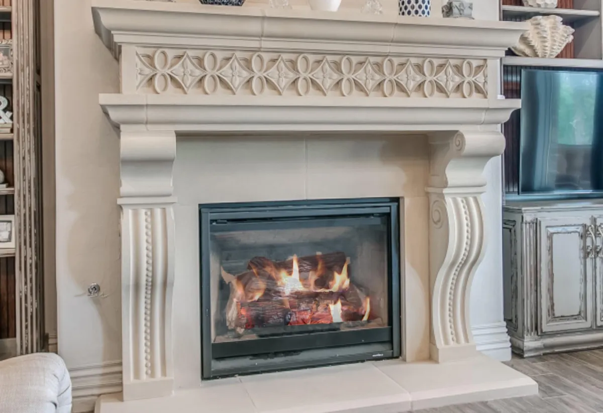The ornate Bella Gamba stone fireplace, showcasing intricate floral carvings and its signature, beautifully curved support leg.