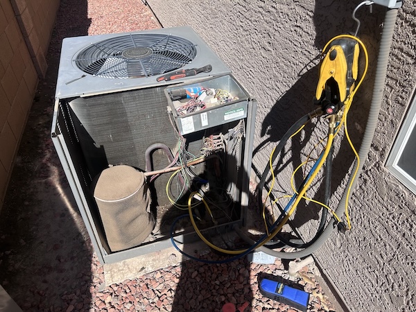 AC condenser unit with access panel open and refrigerant gauges connected during an emergency diagnostic