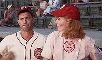 A baseball player glances sideways with a skeptical, unimpressed expression while a teammate in a matching uniform talks beside him in the dugout during a game.