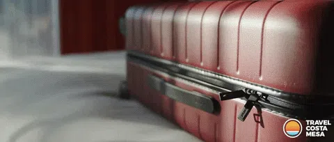 Close-up of a red hard-shell suitcase with a broken zipper pull and partially open zipper, resting on a luggage conveyor belt
