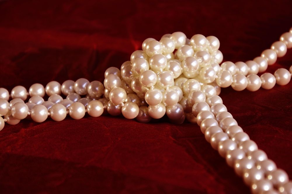 Several strands of white pearls tangled together on a deep red velvet background.