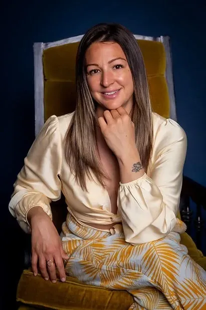 Sheena Dressel in cream blouse and patterned skirt reflects deeply, embodying resilience and transformation with Evolved Being.