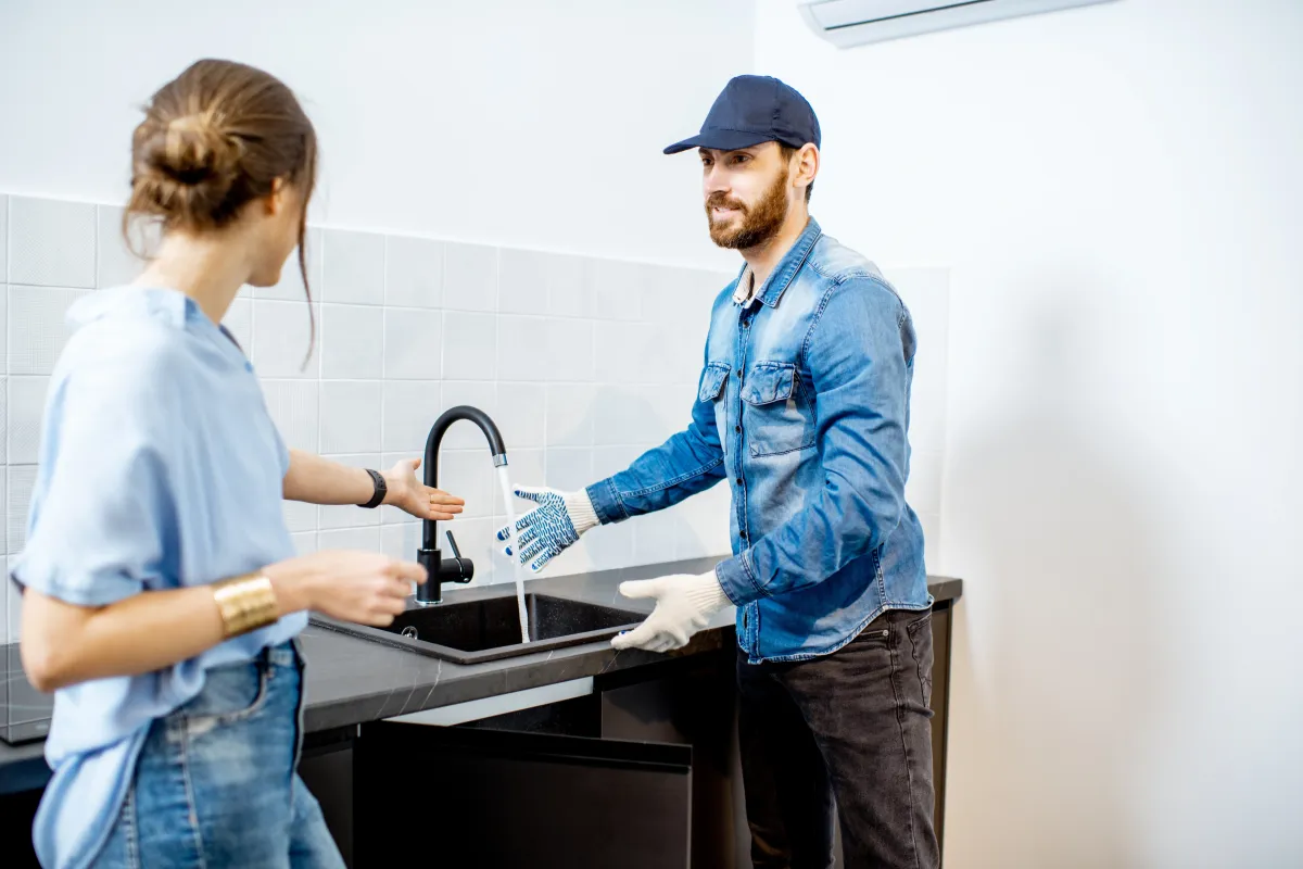 Plumber testing a repaired kitchen faucet with a homeowner after fixing a leak.