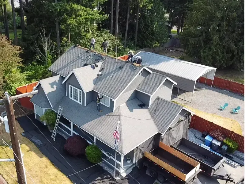 Aerial view of a reroof in progress with a dump trailer staged in the driveway for tear-off debris