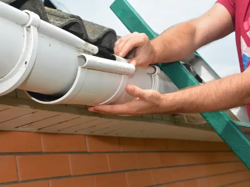 Close-up of hands fitting a downspout section onto a gutter pipe.