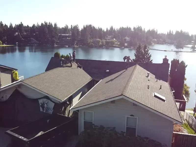 Roofers completing roof replacement on lakeside home.