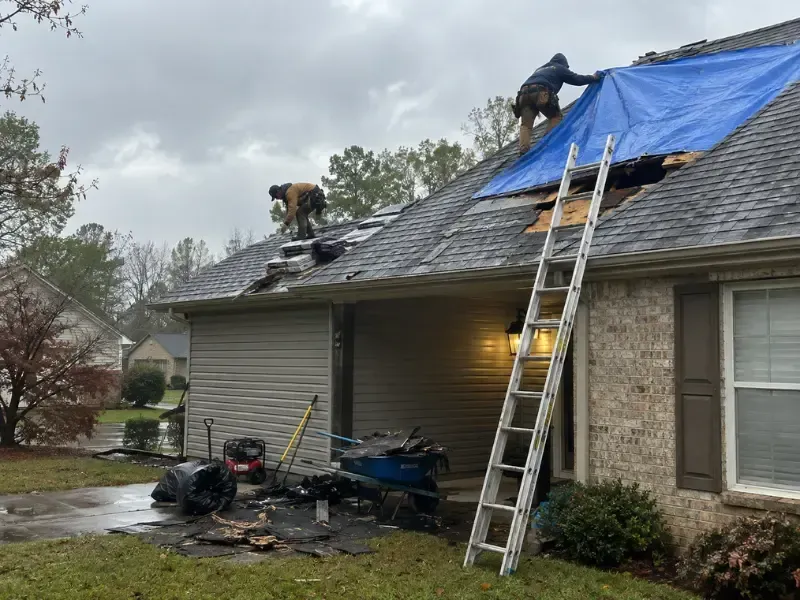 Roofing crew covering storm-damaged shingles with a blue tarp on a residential roof to prevent water intrusion.