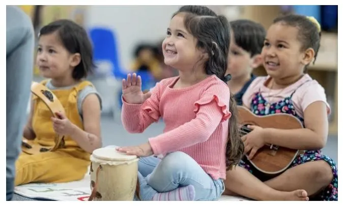 Boy holding a tambourine while watching the teacher on his tablet