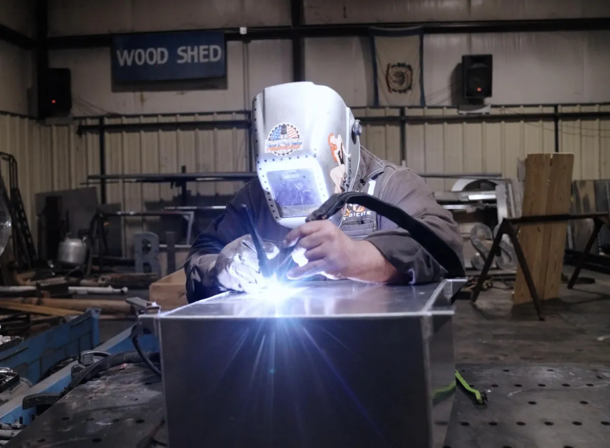 Welder in a welding mask working on metal with a bright welding arc at CNC Syndicate's shop in Ravenswood, WV, showcasing professional welding and fabrication services