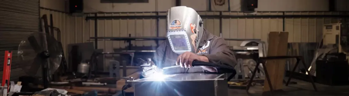 Welder in a welding mask working on metal with a bright welding arc at CNC Syndicate's shop in Ravenswood, WV, showcasing professional welding and fabrication services