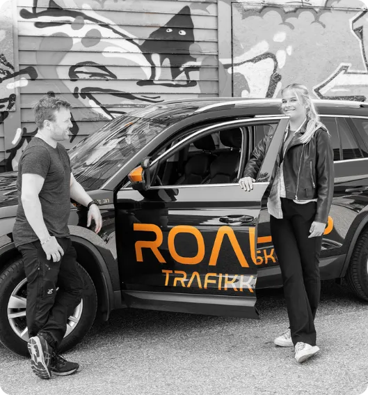 Kjørelærer ved Roalds Trafikkskole står ved skolebilen i Bergen sammen med elev.